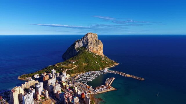 Calpe coastline in Spain featuring the iconic Penon de Ifach rock formation rising from the Mediterranean Sea alongside a marina and urban waterfront buildings