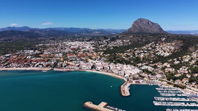 Javea coastal town on Costa Blanca Spain with turquoise Mediterranean bay, marina with moored boats, white buildings and dramatic rocky mountain backdrop