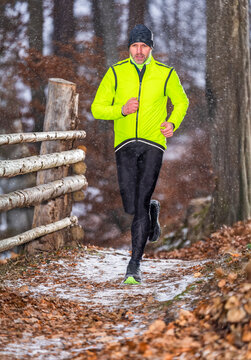 Man trail running on a snow-covered forest path in winter