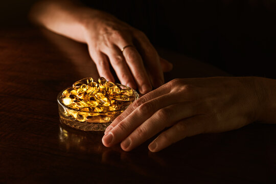 Hands by a bowl of omega 3 capsules on a wooden table indoors