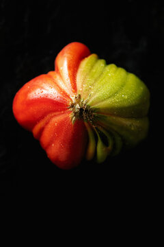 Wet organic heirloom tomato directly above on black background
