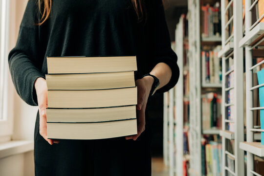 Student holding a stack of books in a library