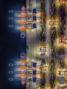 Aerial overhead view of a illuminated container terminal dock with loading and unloading activity by cranes and trucks off cargo ships