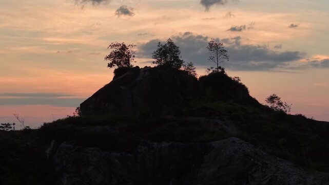 Aerial silhouette of Frog Hill in Kubang Semang during sunset with trees and rock formations.