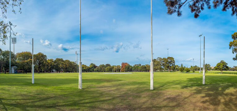 The iconic white AFL goal posts stand tall at Ikon Park (Princes Park) in Carlton, Melbourne, set against a backdrop of lush green turf on a bright, clear afternoon.