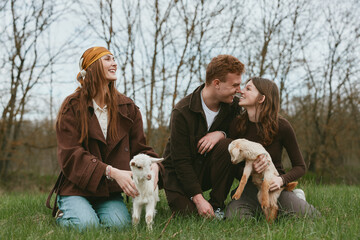 Fototapeta premium Three friends outdoors with dogs enjoying a relaxed moment in a grassy park, warm brown tones, casual outfits, natural light, candid interaction, and a sense of companionship