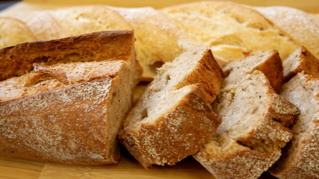 Fresh white and dark baguettes on a table, one loaf sliced into pieces. Panorama composition. Concept of bakery products, fresh bread, food presentation, and daily nutrition. Rustic style, natural