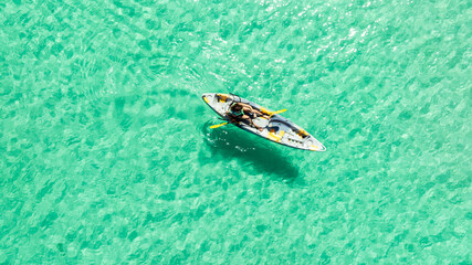 Naklejka premium High angle aerial view of a woman paddling a kayak in crystal clear turquoise ocean water near a tropical white sand beach with palm tree shadows, concept of summer luxury vacation and travel. 