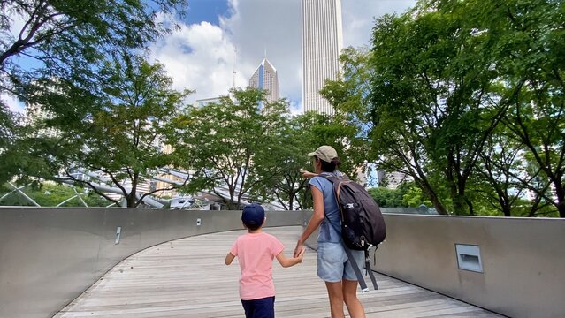 Mother and child enjoying a family day out, walking on a pedestrian bridge in millennium park, chicago, observing the urban skyline and city skyscrapers