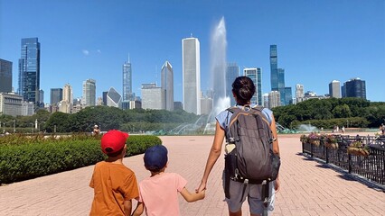 Obraz premium Family exploring chicago city skyline, seeing buckingham fountain with mother holding hands of two children, enjoying urban tourism and summer travel in grant park