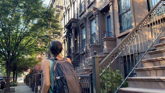 Young woman walking along a tree-lined street in harlem, new york city, exploring cultural heritage and urban architecture with historic brownstone buildings