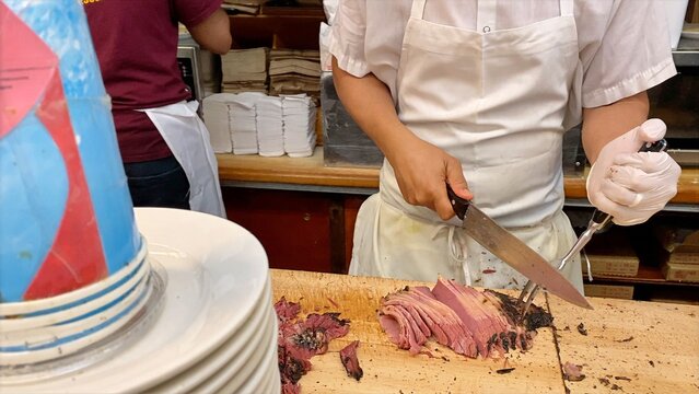 Chef slicing hot pastrami meat by hand on a wooden cutting board, preparing a classic new york city deli sandwich, showcasing traditional food preparation