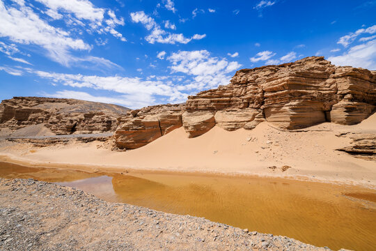 Arid desert landscape with rock formations and reflection on water under blue sky in Xinjiang, China