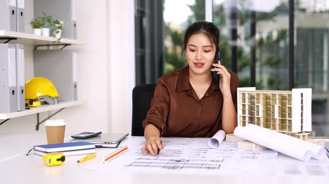 Female Civil Engineer Construction professional reviewing shop drawing of structural floor plan  and communicates on smartphone in an office.
