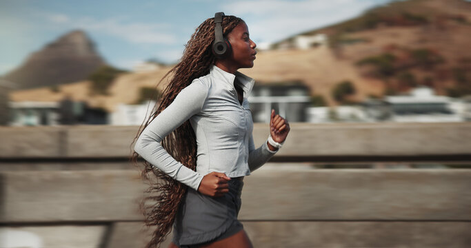 Fitness, woman and running with headphones in city for speed challenge, cardio and interval training. Fast athlete, black person and sprint on bridge for exercise, sport performance and workout music