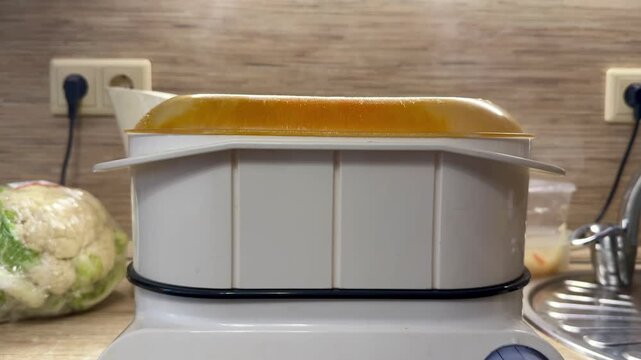 Yellow steamer lid steaming on countertop electric steamer bubbling while vegetables cook, condensation beading on plastic lid