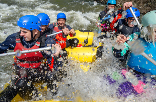 Rafting - water is splashing in to the boat while six excited people with water gear are rowing down the white water river
