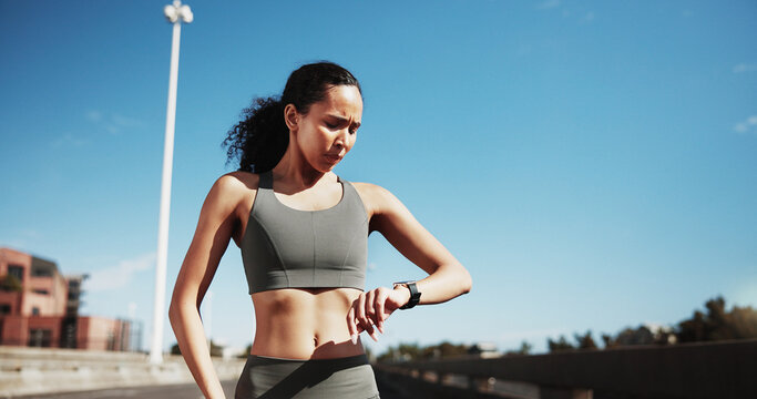 City, runner and woman with watch for exercise progress, health app and fitness tracker outdoor. Sports, blue sky and person check time for training, workout and active hobby for wellness in town