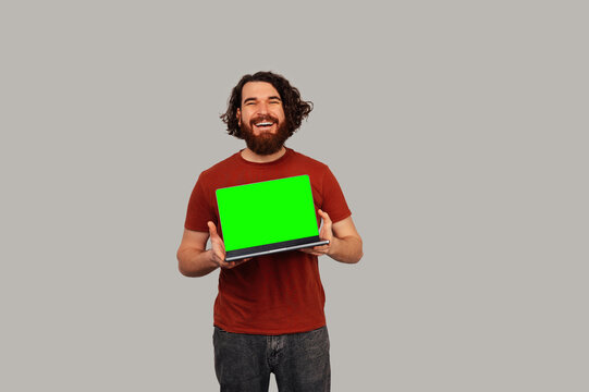 White Man Holding Green Laptop Smiling At Camera, Casual Red Shirt, Studio Grey Background, Confident Product