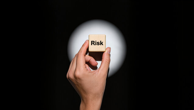 Hand Holding Wooden Cube with "Risk" Text Against Spotlight