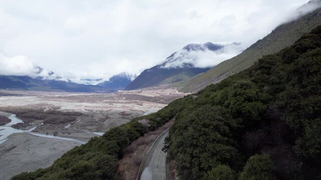 Drone view of road through village in Bomi County, Nyingchi, Tibet, China. Beautiful pink peach blossoms with snow covered mountains and white clouds background. 4k real time footage, travel concept.