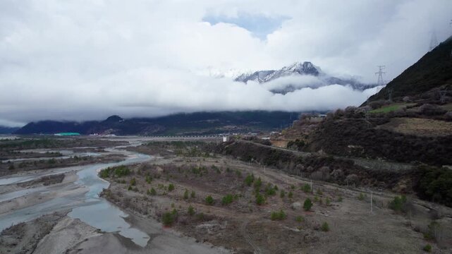Drone view of village in Bomi County, Nyingchi, Tibet, China. Beautiful pink peach blossoms with snow covered mountains and Parlung Zangbo river background. 4k real time footage, travel concept.