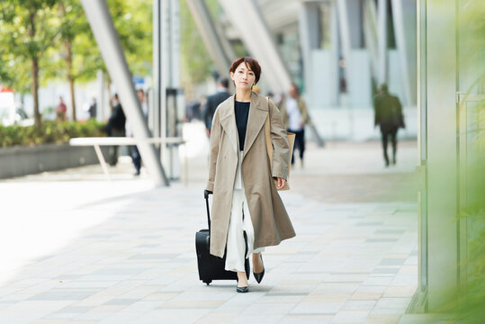トレンチコートを着てキャリーバッグを引く30代ビジネス女性