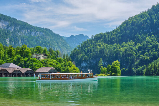 Scenic landscape of an electric boat on the Konigsee lake with boathouses on the shore and lush Alpine mountains in Berchtesgaden, Bavaria, Germany.
