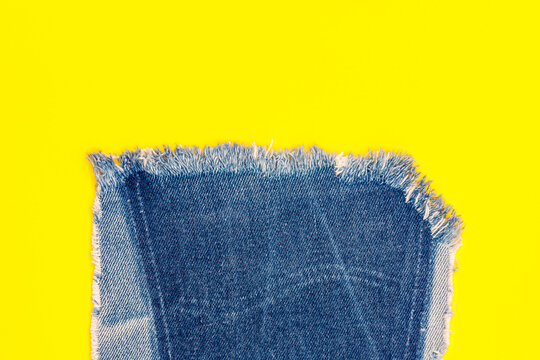 Blue denim fabric piece on bright yellow background showing texture and edge details