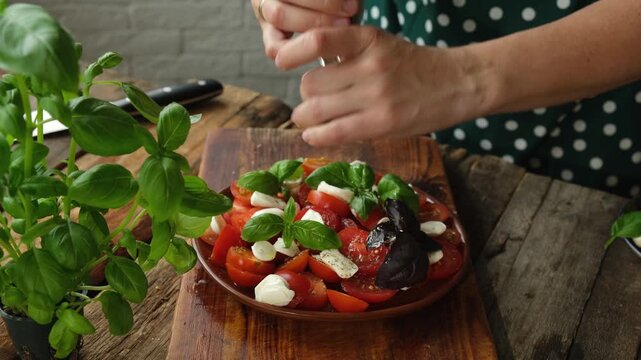 Preparation of caprese salad. Adding spices to caprese salad made of chopped tomatoes, mozzarella and basil.