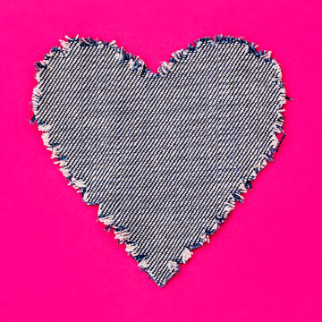 Heart shape made from denim fabric on bright pink background with simple design