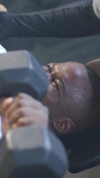 Male lifter gripping dumbbells initiating press, male spotter steadying wrists for safe fitness rep