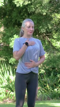 Vertical video: Seeing motion woman tied tee holding chest and belly calming breaths in garden band