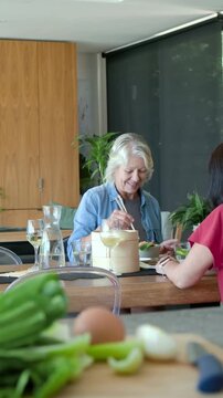Vertical video: Senior woman reaching steamer, serving, eating with chopsticks, chatting about food