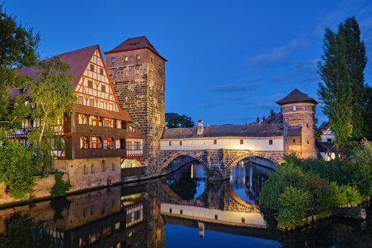 Beautiful twilight view of the illuminated Henkersteg bridge and half-timbered houses reflecting in the Pegnitz river in Nuremberg, Germany.