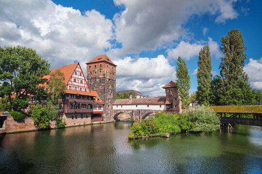 Wide angle view of the medieval riverside architecture in Nuremberg, featuring the Hangman's bridge and Weinstadel under a blue sky.