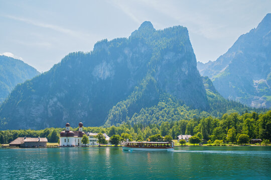Electric passenger boat cruising the emerald waters of Lake Konigssee with St. Bartholoma pilgrimage church and Watzmann mountains in Bavaria, Germany