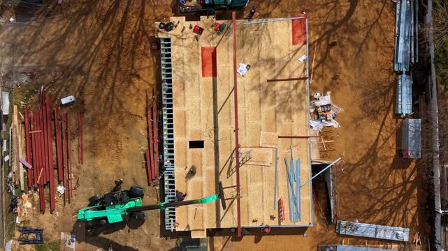 Aerial timelapse straight down over new home construction in a middle-class suburban neighborhood on a sunny day, capturing workers on site. The camera tilted down, zoom in towards site and workers.