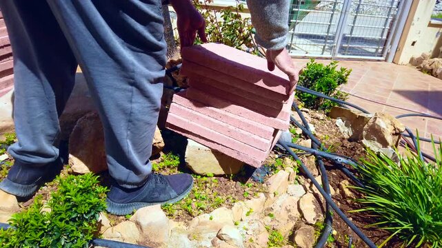 Man arrives at front garden to take a red pathing stone away from pile, garden maintenance, moving techniques, groundsman working for home improvement.