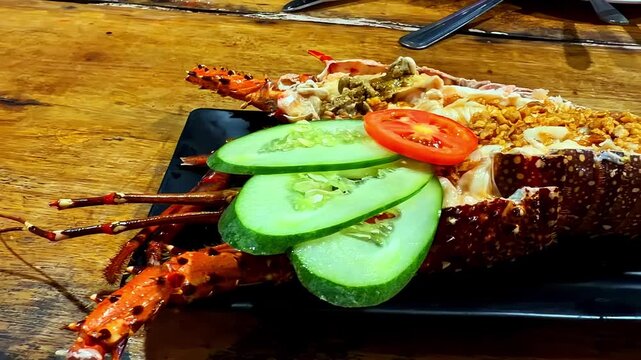 Stuffed lobster served in its shell with cucumber slices, tomato garnish, and crunchy garlic topping on a black plate in a casual seafood restaurant.