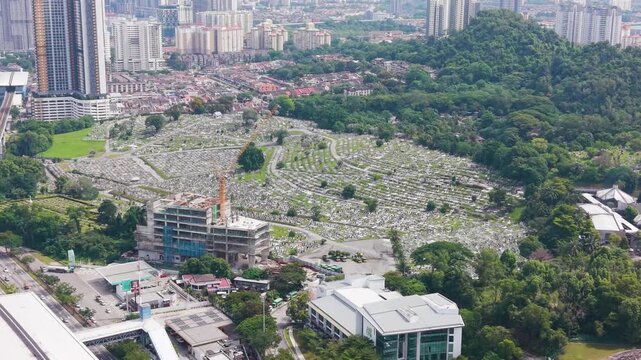 Aerial view of Cheras War Cemetery in Kuala Lumpur, Malaysia, showing organized graves, green surroundings, and an urban skyline blending history with modern city landscape. UHD.