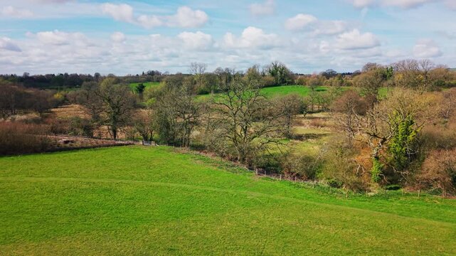 Low altitude aerial drone footage of farmland field and surrounding trees in rural Wiltshire England showing natural landscape and agricultural environment