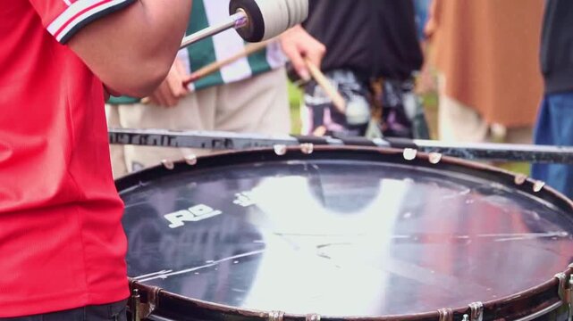 Close-up of a drummer hitting a large drum with mallets. Energetic rhythm performance at an outdoor event, perfect for music and festival themes.