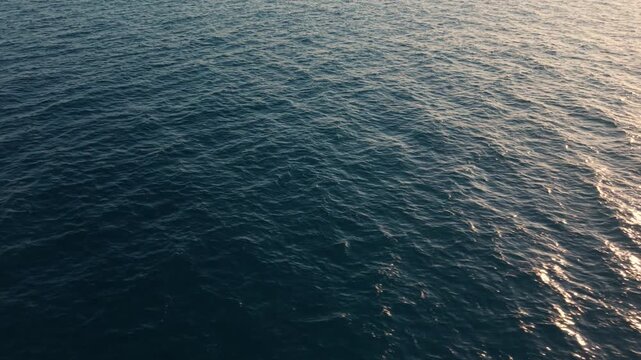 Drone flying above ocean surface with sunlight reflections on waves creating abstract water texture