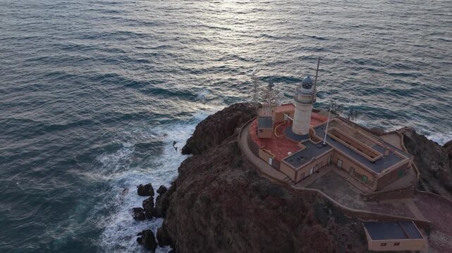 Cinematic aerial perspective of the iconic Cabo de Gata lighthouse perched on a dramatic cliff with waves breaking against the rocks