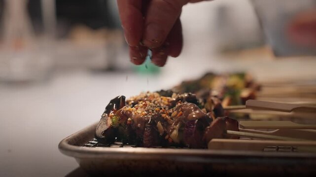 Sesame seeds are sprinkled onto a tray of vegetable skewers (slow motion 4K).