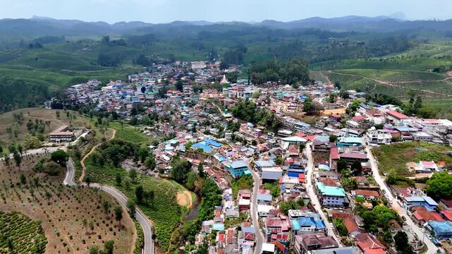 Drone shot capturing a lively hillside settlement featuring mixed residential and commercial structures, winding streets, and a central landmark, with lush green landscapes stretching into the distanc