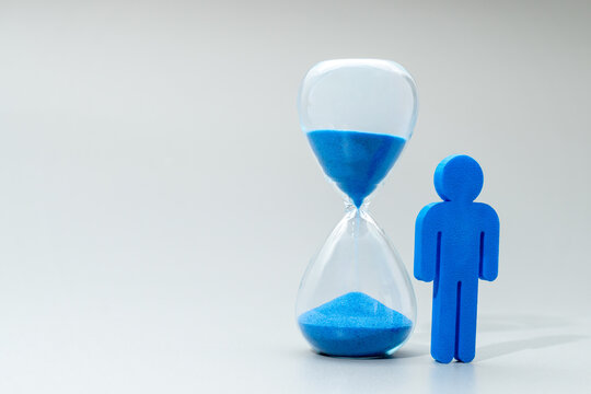 A blue miniature human figure and hourglass. Time management, aging, male mortality, life expectancy concept.