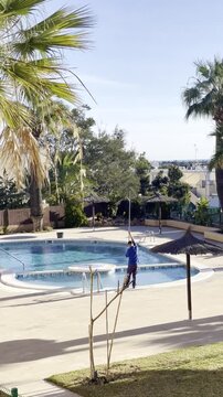 Socorrista en mantenimiento de piscina y limpieza con palo limpiafondos en verano 