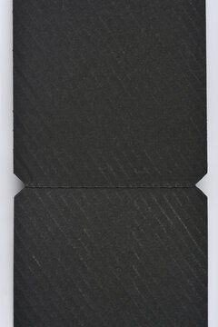A close up of black textured paper featuring a diagonal ribbed pattern and a horizontal perforated line with side notches